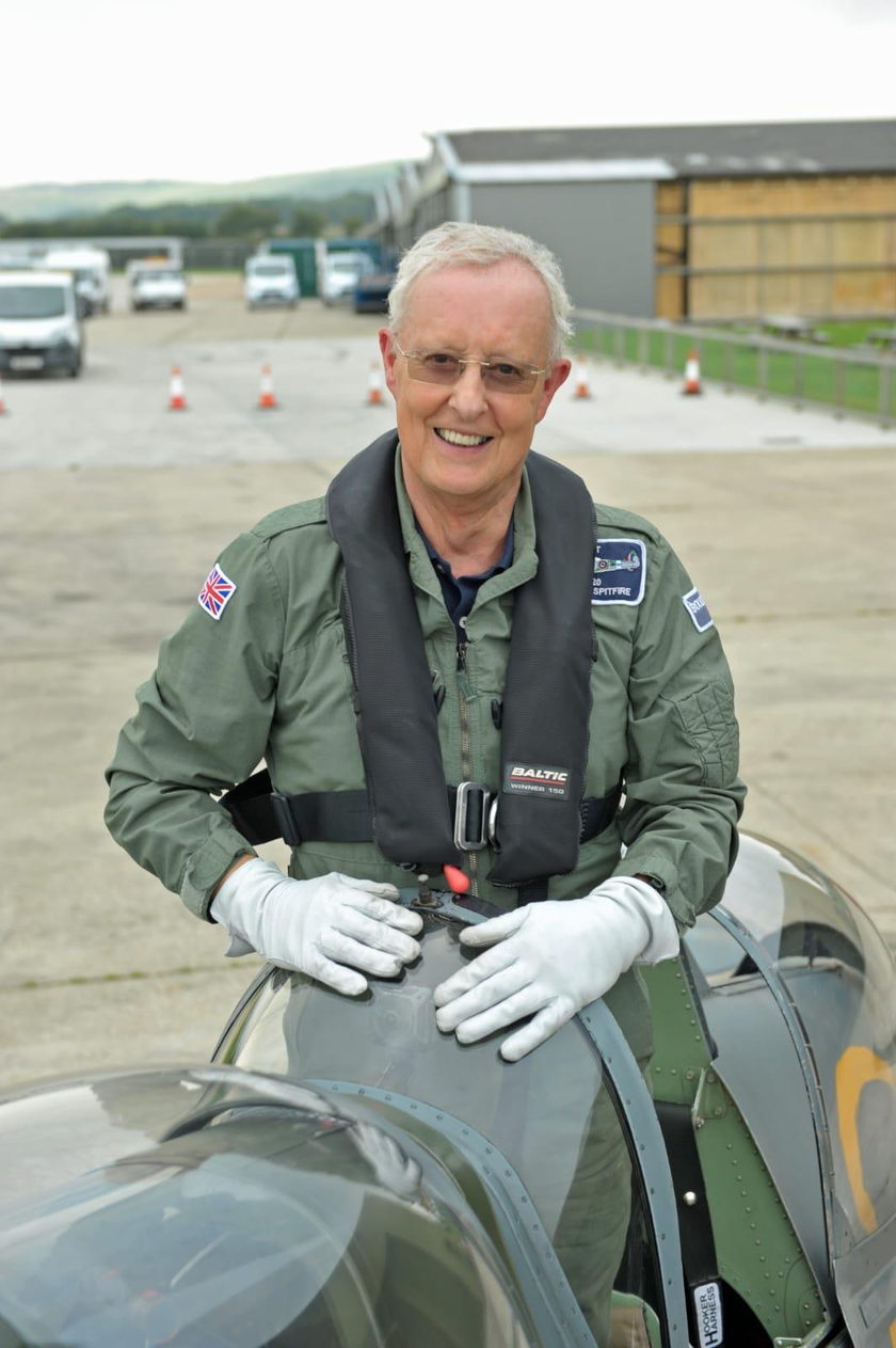 Richard Sumner in a flying suit and life jacket, smiling, leaning on the cockpit of a Spitfire